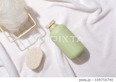 A bath sponge in an iron basket, a bar of soap and an unlabeled bottle of shower gel are displayed on a white fabric background. Minimalist space for advertising. A bath sponge in an iron basket, a bar of soap and an unlabeled bottle of shower gel are displayed on a white fabric background. Minimalist space for advertising. 109750740