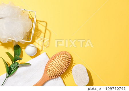 A bath sponge in an iron basket, green leaves, white ball, a towel, soap and a detangling comb are decorated in the left corner on a yellow background. Free space for product design and display. A bath sponge in an iron basket, green leaves, white ball, a towel, soap and a detangling comb are decorated in the left corner on a yellow background. Free space for product design and display. 109750741