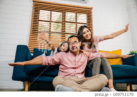 In their modern home an interracial family enjoys quality time together playing plane games with their daughter. Smiles laughter and togetherness fill the room with happiness. 109751170