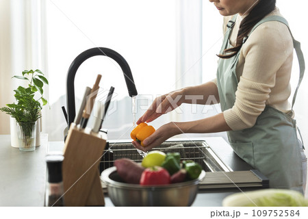 パプリカを水で洗うエプロン姿の女性 109752584