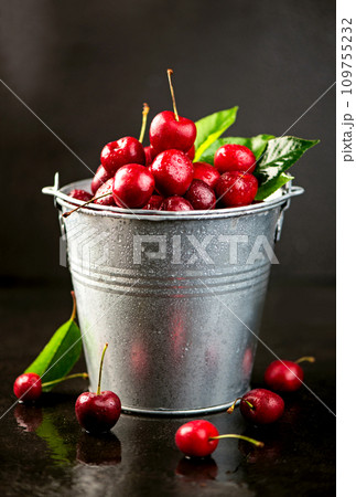 Preparing cherries for jam. Ripe sweet cherry berry with leaves in a bucket on a black wooden board 109755232