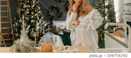 Woman Kitchen Christmas decor in white shirt, peeling tangerines. Illustrating New Year's mood holiday preparations Woman Kitchen Christmas decor in white shirt, peeling tangerines. Illustrating New Year's mood holiday preparations 109756292