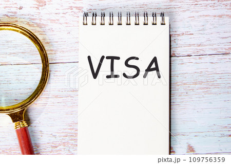 VISA a word written on a notebook on wooden boards next to a magnifying glass VISA a word written on a notebook on wooden boards next to a magnifying glass 109756359