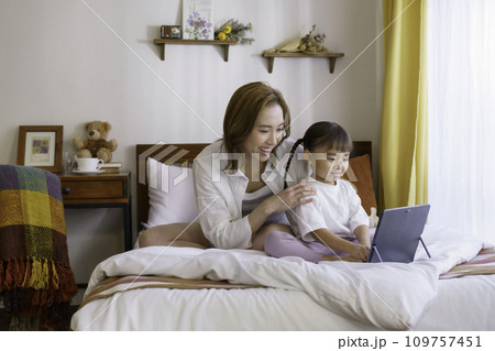 ベッドの上で子供とタブレットを見る若いママ ベッドの上で子供とタブレットを見る若いママ 109757451