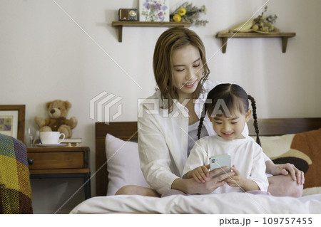 ベッドの上で子供とスマホを見る若いママ 109757455