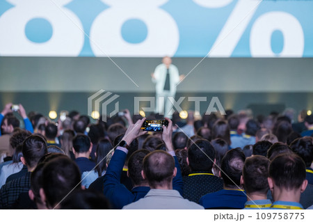 Back view of businesspeople listening to male speaker on stage during global presentation at conference hall  109758775