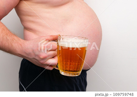 A pot-bellied man holds a mug of beer in his hand. Isolated on a white background. A pot-bellied man holds a mug of beer in his hand. Isolated on a white background. 109759748