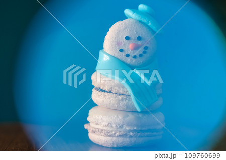 Snowman macaron dessert decorated with hat and scarf inside abstract blue snow globe. Merry Christmas and Happy New Year festive concept 109760699