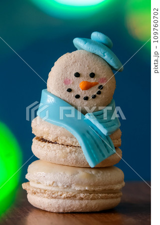 Snowman macaron dessert decorated with hat and scarf against colorful lights and bokeh background. Merry Christmas and Happy New Year festive concept 109760702