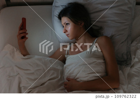 Young woman laying in bed and using her smartphone at night. Young woman laying in bed and using her smartphone at night. 109762322