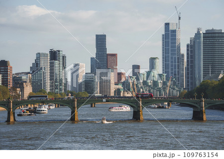 Distant view of vehicles on Westminster bridge. Boats moving on Thames river with modern buildings in background. Scenic urban beauty of capital city in London. 109763154