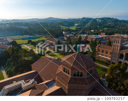 Aerial view of UCLA campus highlighting Romanesque Revival architecture, lush greenery, and red-tiled roofs under a clear blue sky in Westwood, Los Angeles. Aerial view of UCLA campus highlighting Romanesque Revival architecture, lush greenery, and red-tiled roofs under a clear blue sky in Westwood, Los Angeles. 109763257