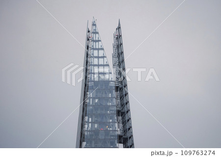 Top view of The Shard in city. Financial office building with cloudy sky in background. Glass windows on modern artistic structure in London. Top view of The Shard in city. Financial office building with cloudy sky in background. Glass windows on modern artistic structure in London. 109763274