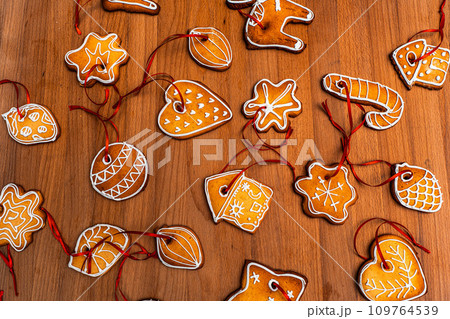 Wooden background with lots of gingerbread Christmas gingerbread in the shape of a house, heart. Deer. star, christmas tree toy, ball with white glaze. High quality photo 109764539