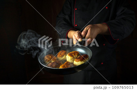 The chef fries donuts in a frying pan. The concept of preparing a Polish national dish in a restaurant kitchen. Black space for recipe or menu 109765013