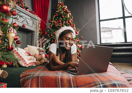 Young African woman on bed using laptop on Christmas eve Young African woman on bed using laptop on Christmas eve 109767652
