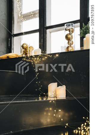 Black windowsill decorated for Christmas with golden baubles and candles Black windowsill decorated for Christmas with golden baubles and candles 109767895