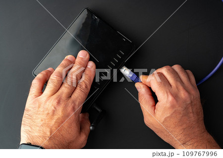Man's hand plugging internet cable into wifi router Man's hand plugging internet cable into wifi router 109767996