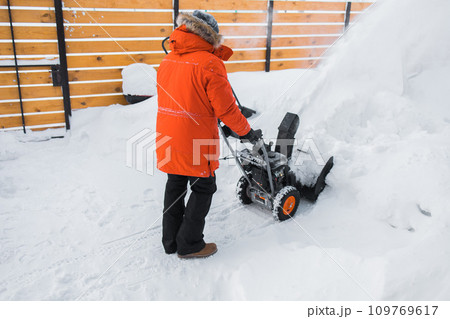 A man clear snow from backyard with snow blower. Winter season and snow blower equipment 109769617