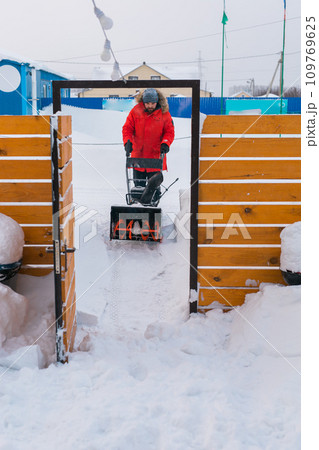 A man clear snow from backyard with snow blower. Winter season and snow blower equipment A man clear snow from backyard with snow blower. Winter season and snow blower equipment 109769625