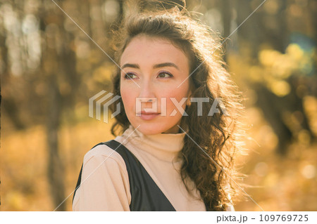 Attractive young woman walking in autumn park, happy mood and fashion style trend and curly long brown hair. Fall season and pretty female portrait copy space. Millennial generation concept Attractive young woman walking in autumn park, happy mood and fashion style trend and curly long brown hair. Fall season and pretty female portrait copy space. Millennial generation concept 109769725