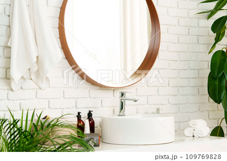 Bathroom interior with circle shaped mirror in wooden frame and white sink 109769828
