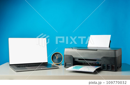 Modern printer with paper and laptop on table in office 109770032