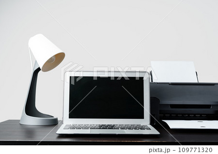 Modern printer with paper and laptop on table in office 109771320