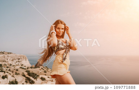 Woman travel sea. Happy tourist taking picture outdoors for memories. Woman traveler looks at the edge of the cliff on the sea bay of mountains, sharing travel adventure journey 109771888