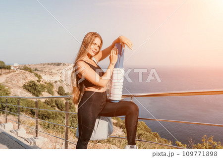 Fitness woman sea. Outdoor workout on yoga mat roller in park near to ocean beach. Female fitness pilates yoga routine concept. Healthy lifestyle. Happy fit woman exercising with rubber band in park. 109771898