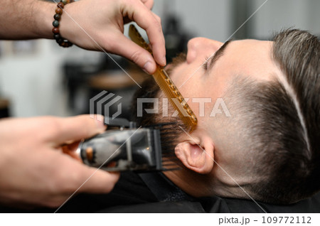 Barber combs beard with comb while shaving Caucasian man 109772112