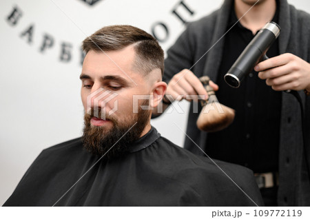 The hairdresser sweeps the hair during the haircut with a brush and drying air. The hairdresser sweeps the hair during the haircut with a brush and drying air. 109772119