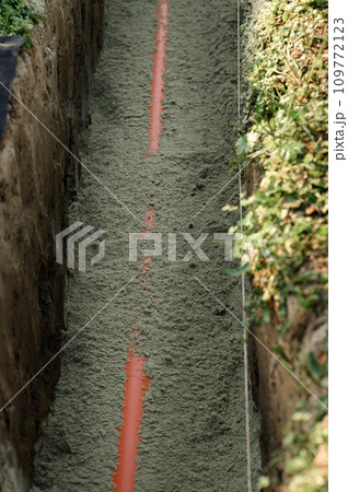 An orange reinforced sewer pipe is compacted with sand in a trench. Plumbing works on private plot. 109772123