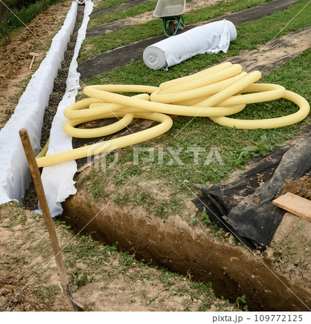 Yellow corrugated pipe with perforation in a trench with crushed stone and geotextile. Drainage works for the removal of ground water. 109772125