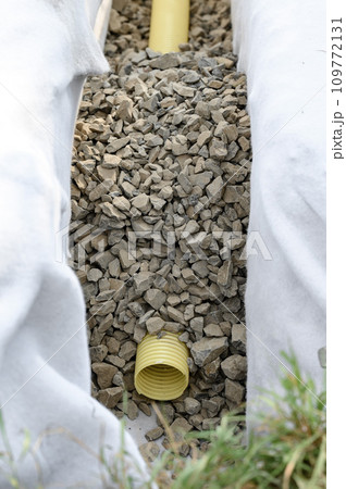 Yellow corrugated pipe with perforation in a trench with crushed stone and geotextile. Drainage works for the removal of ground water. Yellow corrugated pipe with perforation in a trench with crushed stone and geotextile. Drainage works for the removal of ground water. 109772131