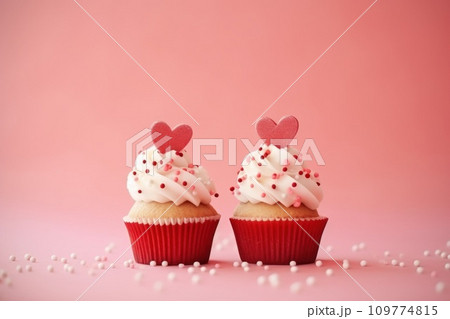 AI-generated content. Valentines Day two cupcakes decorated whipped cream, sprinkles and red hearts isolated on pink background. Greeting card. 109774815