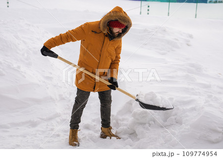 A man cleans and clears the snow in front of the house on frosty day. Cleaning the street from snow on a winter day. Snowfall and severe snowstorm in winter. A man cleans and clears the snow in front of the house on frosty day. Cleaning the street from snow on a winter day. Snowfall and severe snowstorm in winter. 109774954