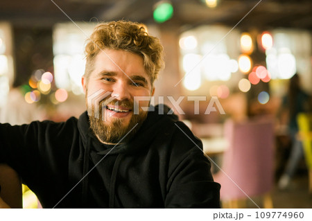 Bearded guy programmer or an entrepreneur in glasses in a stylish cafe looks at the camera and smiles copy space and empty space for advertising. Freelancer works remotely. Online communication video 109774960