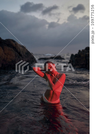 Attractive woman enjoys serene night swim in ocean bathed in red light, embodying tranquil travel and self-care moments at sea. 109775256