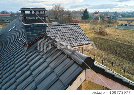 Closeup of house roof top covered with ceramic shingles. Tiled covering of building under construction Closeup of house roof top covered with ceramic shingles. Tiled covering of building under construction 109775977