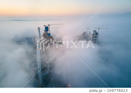 Aerial view of cement factory with high concrete plant structure and tower crane at industrial manufacturing site on foggy evening. Production and global industry concept. 109776023