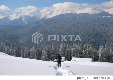 Man backpacker hiking snowy mountain hillside on cold winter day. 109776310