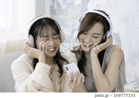 ヘッドホンでスマホの音楽を聴く姉妹 109777155
