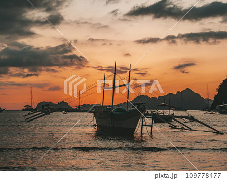Traditional philippine boats bangka at sunset time. Beautiful sunset with silhouettes of philippine boats in El Nido, Palawan island, Philippines. Orange sky sunset paradise beach. Traditional philippine boats bangka at sunset time. Beautiful sunset with silhouettes of philippine boats in El Nido, Palawan island, Philippines. Orange sky sunset paradise beach. 109778477
