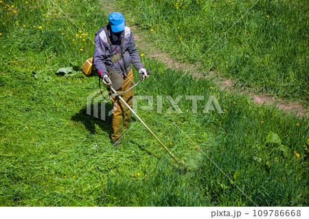 lawnmower man with string trimmer trimming grass at sunny day 109786668