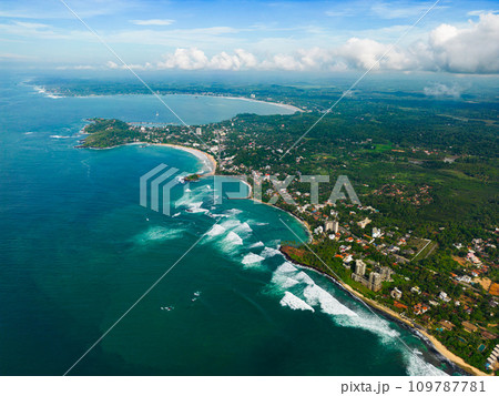 Aerial view with panoramic coastline with sparkling turquoise waters against a lush green landscape, showcasing scenic coastal living and the junction between land and sea from birds-eye perspective. Aerial view with panoramic coastline with sparkling turquoise waters against a lush green landscape, showcasing scenic coastal living and the junction between land and sea from birds-eye perspective. 109787781