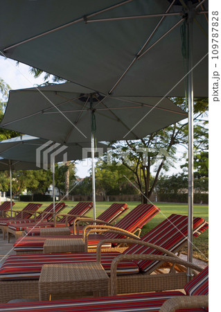 Plastic deck chairs with soft mattresses and umbrellas from the sun stand in a row. Sun loungers for relaxing and sunbathing. Without people. Plastic deck chairs with soft mattresses and umbrellas from the sun stand in a row. Sun loungers for relaxing and sunbathing. Without people. 109787828