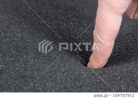 Finger pushing black foam rubber. Closeup full-frame macro view. Finger pushing black foam rubber. Closeup full-frame macro view. 109787911