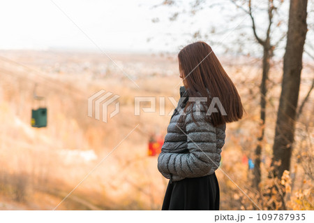 Girl in fall park against background of cable car copy space. Woman with long curly hair. Beautiful sunlight in the forest. Hair care. Generation Z gen z and youth. 109787935