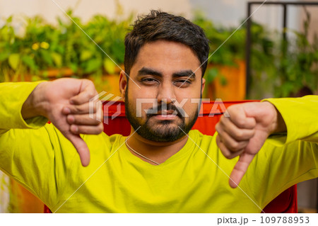Upset Arabian man showing thumbs down, dislike bad work, disapproval dissatisfied feedback at home Upset Arabian man showing thumbs down, dislike bad work, disapproval dissatisfied feedback at home 109788953